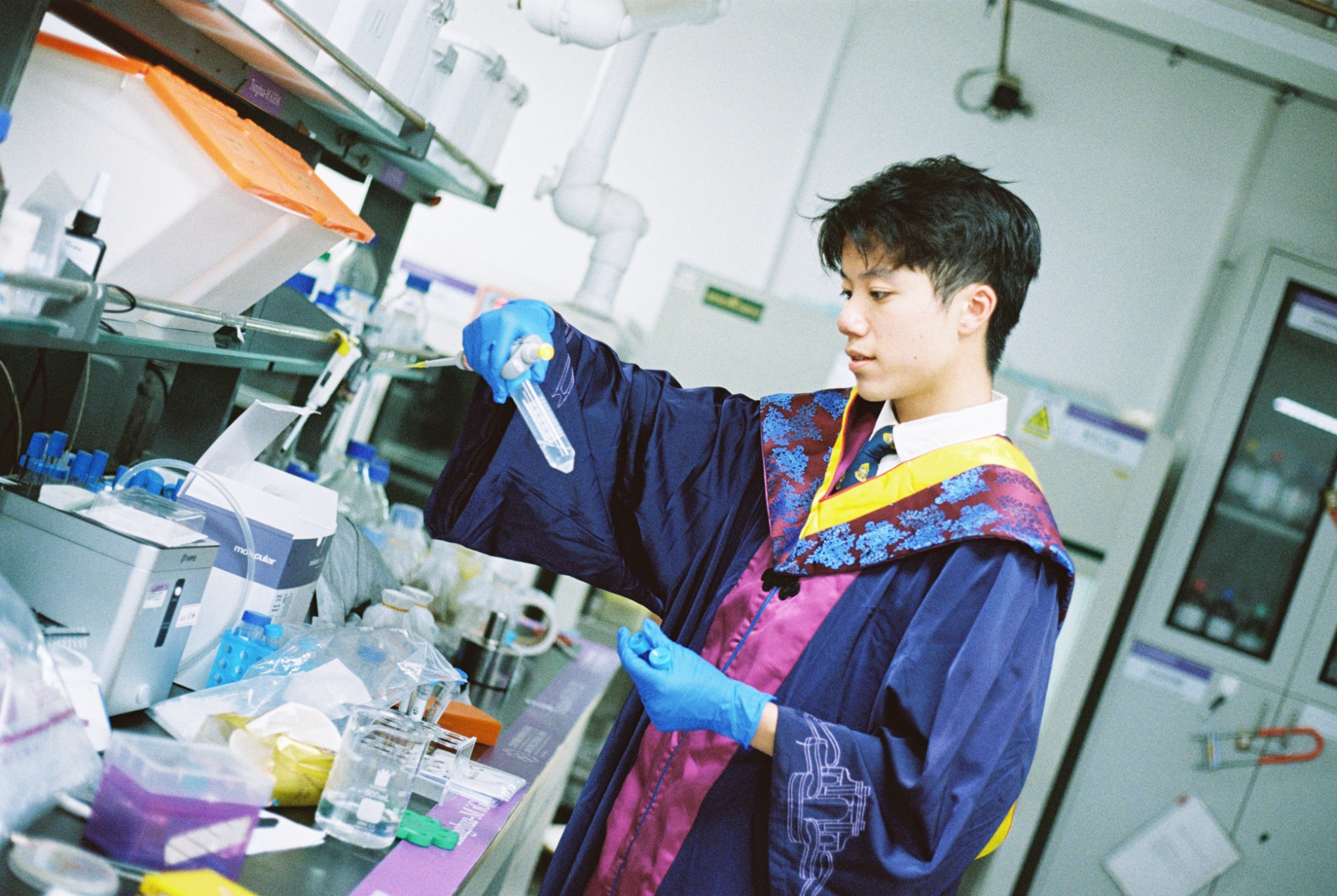 Rico Chi Kit Sou pipetting in the lab in graduation gown